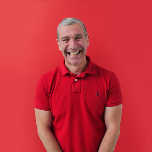 A smiling older man in a red polo shirt against a background of rubies.