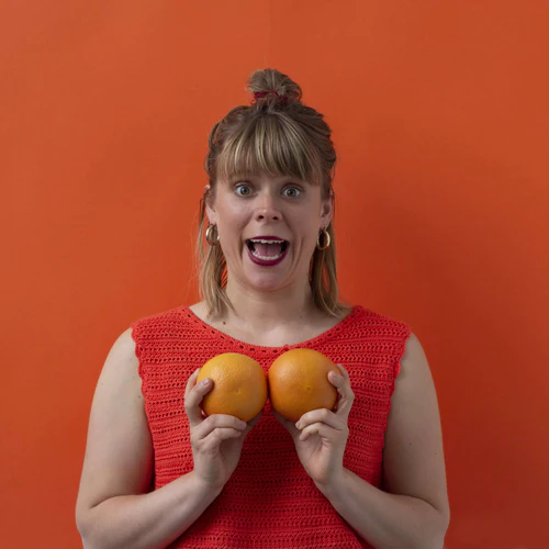 Woman in a red top with a surprised expression, holding two rubies against an orange background.